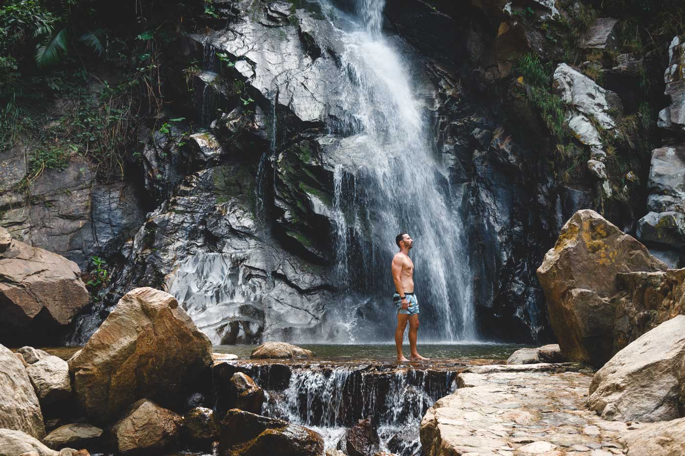 A man posing in front of Yelapa Waterfall in between rocks and the cliff.