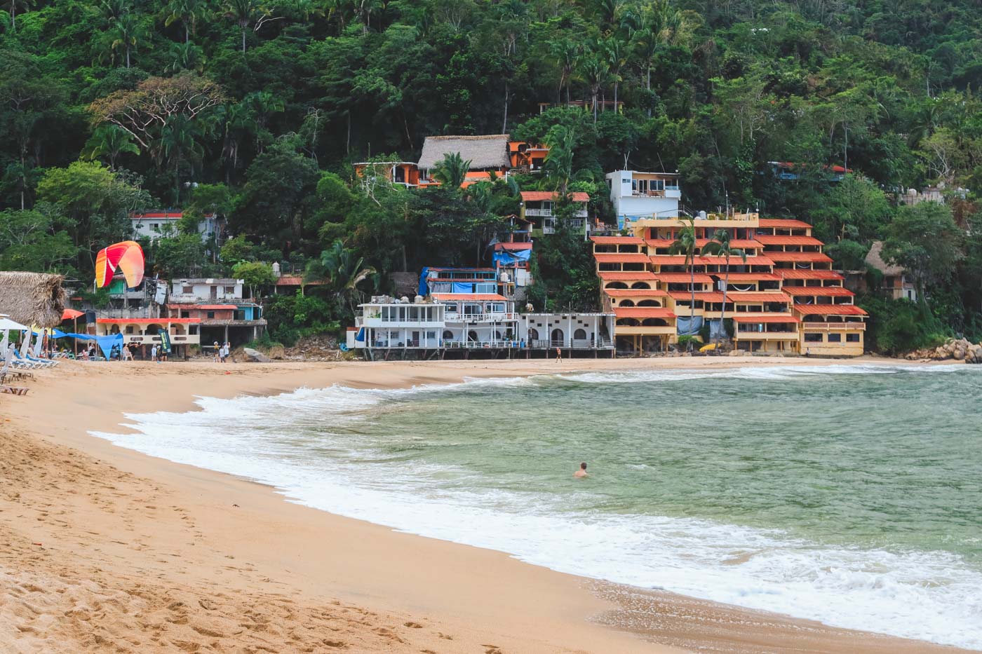 A man swimming in the ocean at an empty Yelapa Beach with a view of hotels in the distance.