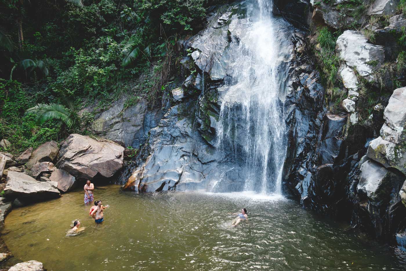 Tourists swimming in the plunge pool at the base of Yelapa Waterfall in the forest.