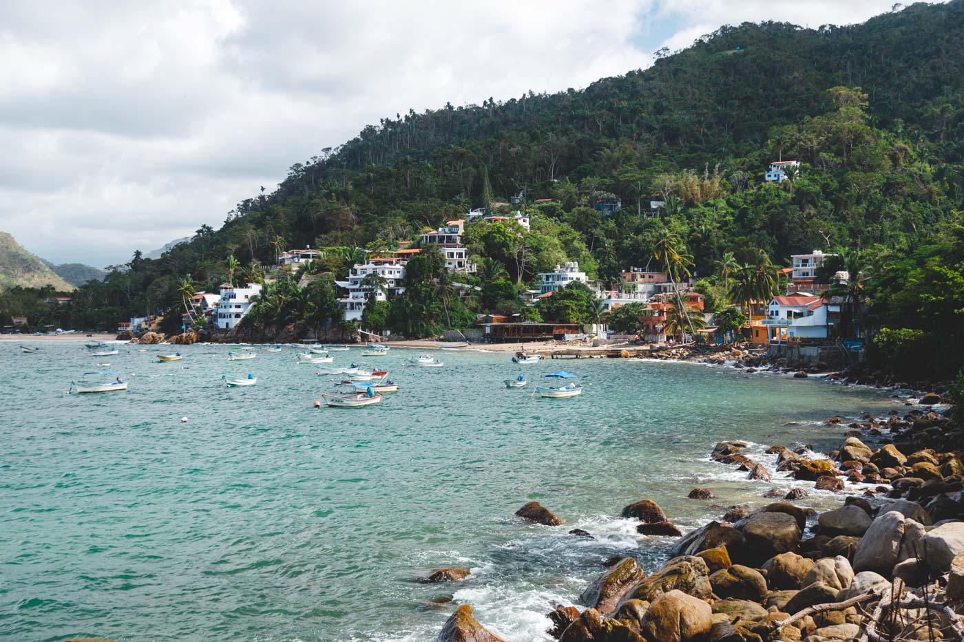 Lots of small boats anchored in a bay near Yelapa Beach with beach villas built into the forests on the mountain.