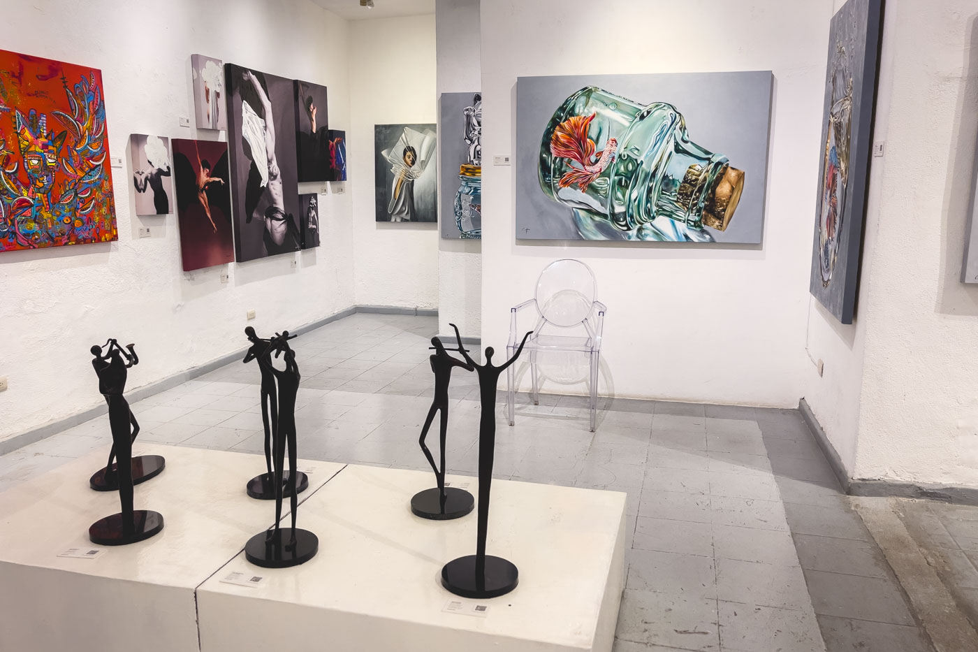 The inside of an art gallery with paintings on the walls and small sculptures on a pedestal.
