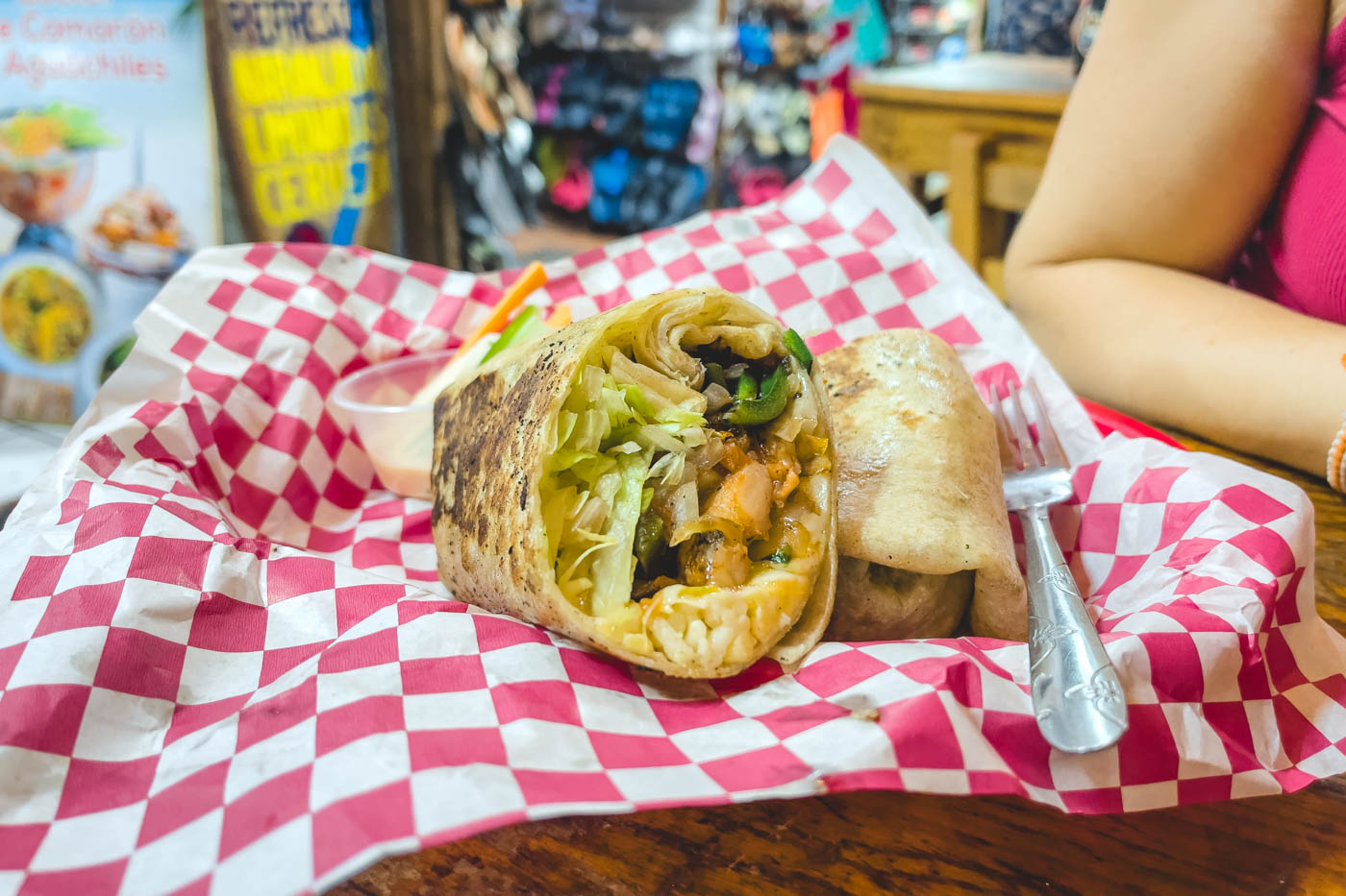 A stuffed burrito laying on a pink and white patchwork sheet in Burrito Beach restaurant.
