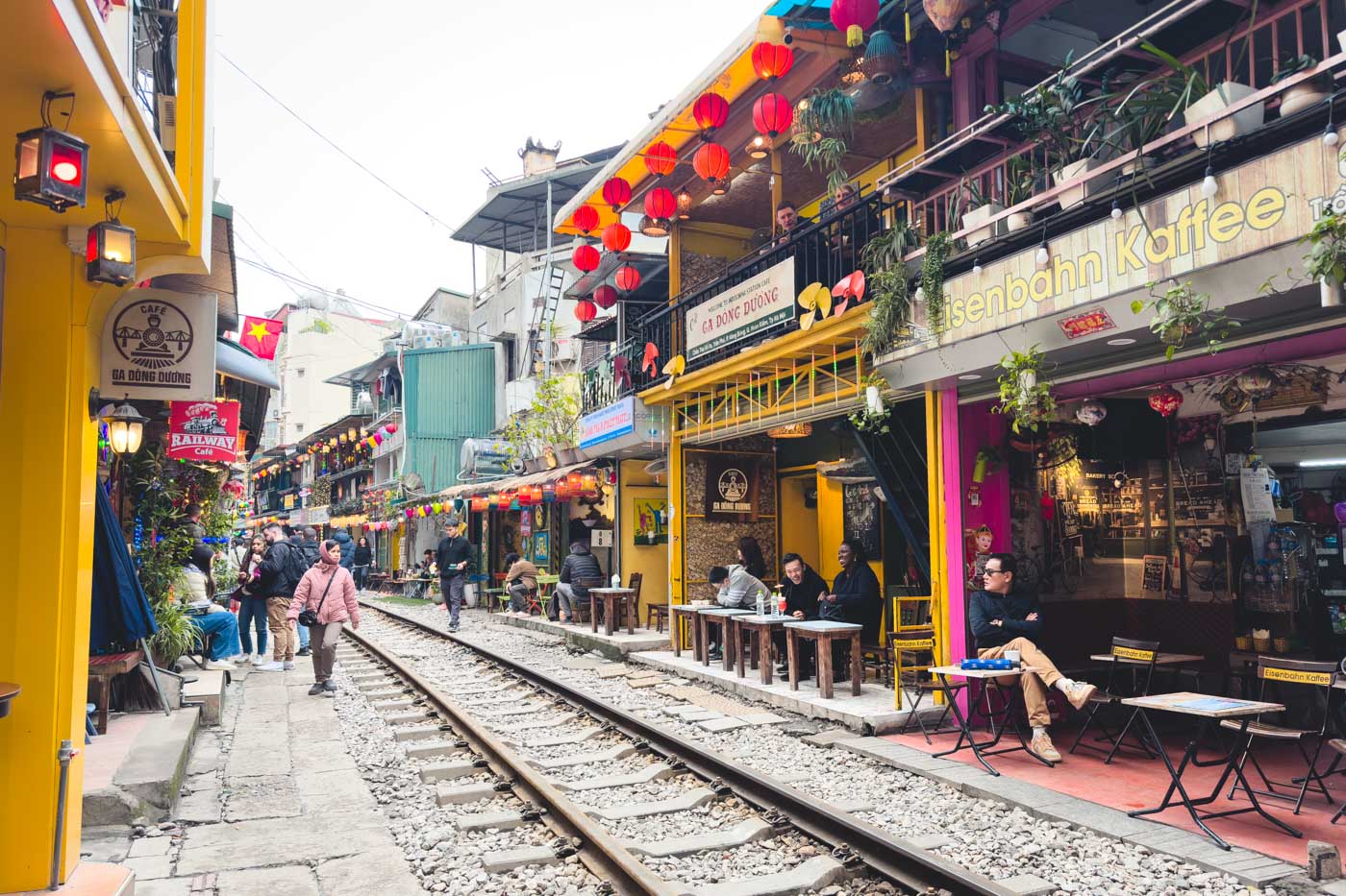 Cafes lining both sides of Hanoi Train Street while people sit inside drinking coffee and waiting for the train.