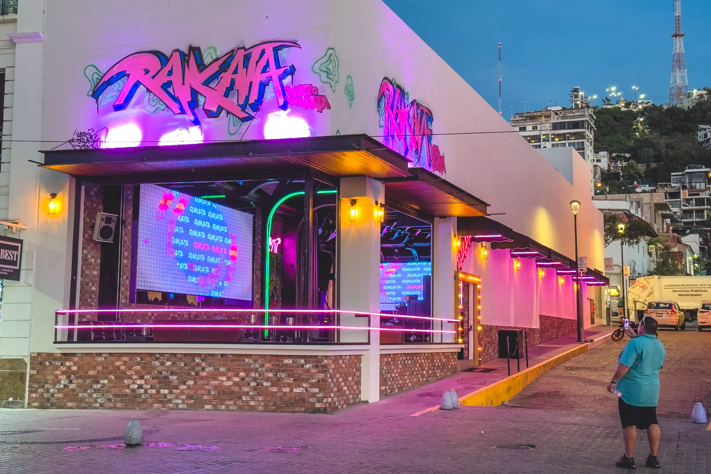 A club in Puerto Vallarta lit up in neon pink and a man in front taking a photo.
