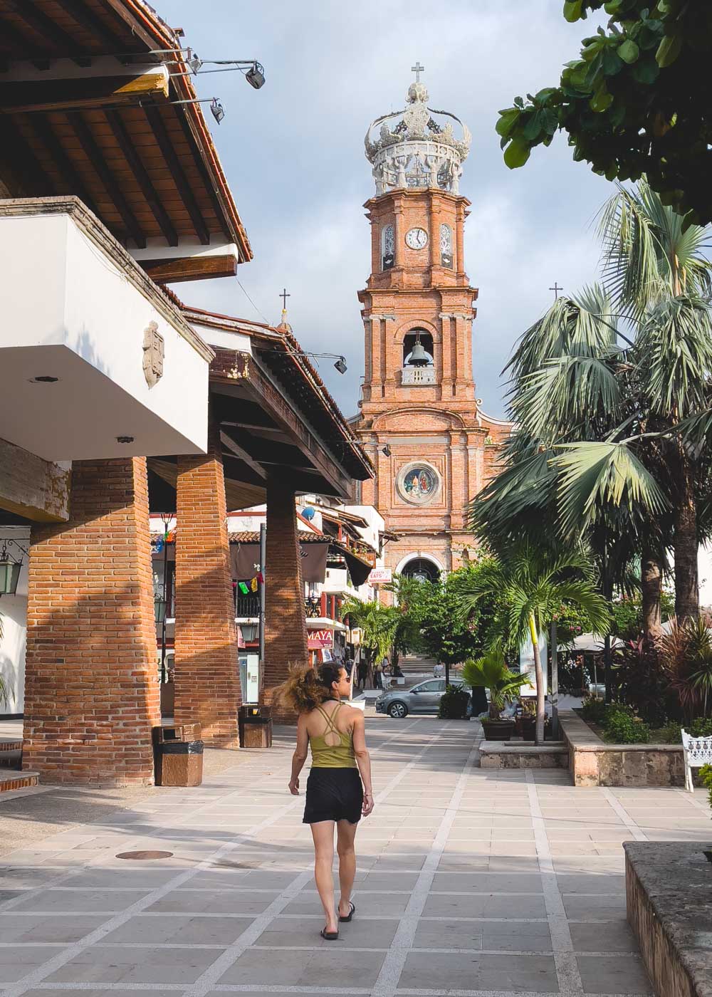 Nina walking between palm trees and buildings heading towards the Church of our Lady Guadalupe in Puerto Vallarta.