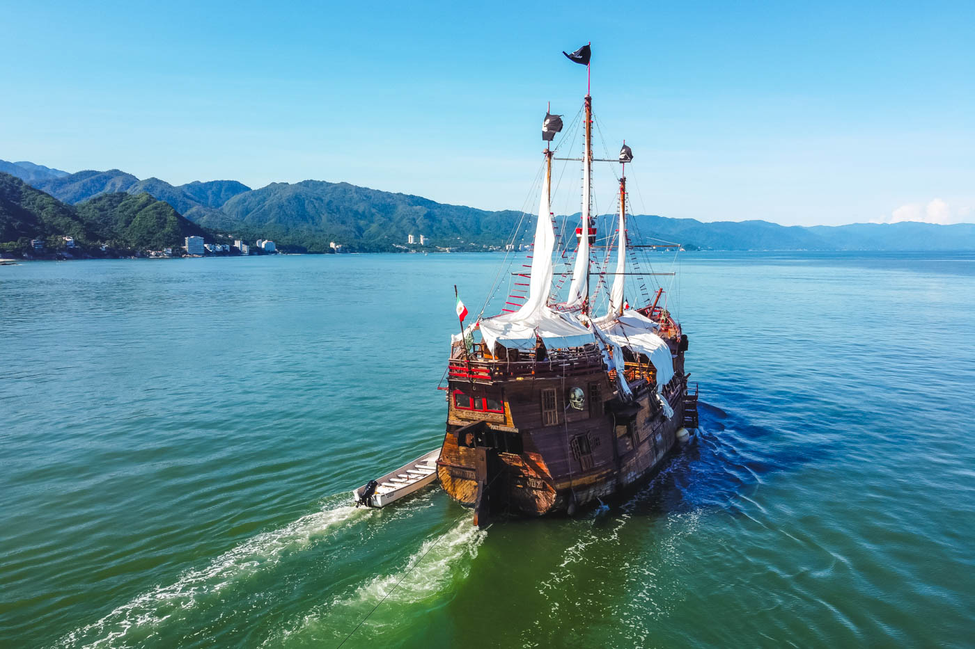 A wooden pirate ship cruising through a bay in Mexico on a sunny day.