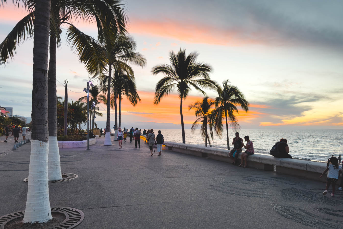 Tourists sitting beside the ocean at sunset along Puerto Vallarta malecon.