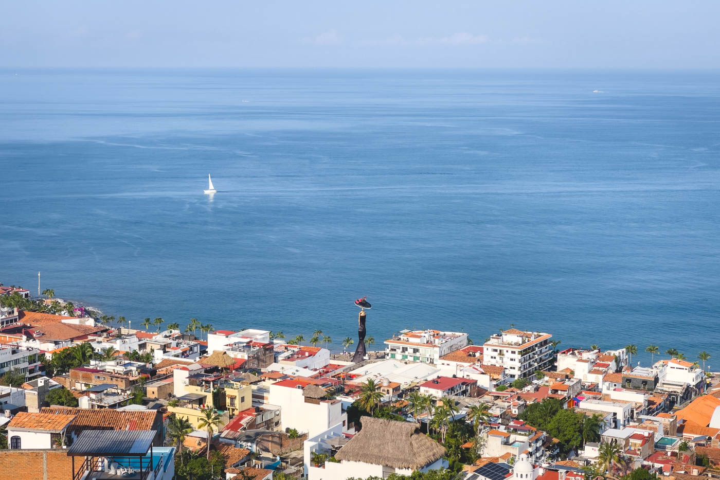 A view over the tallest Catrina statue in all of Mexico in between the buildings of Puerto Vallarta beside the ocean.