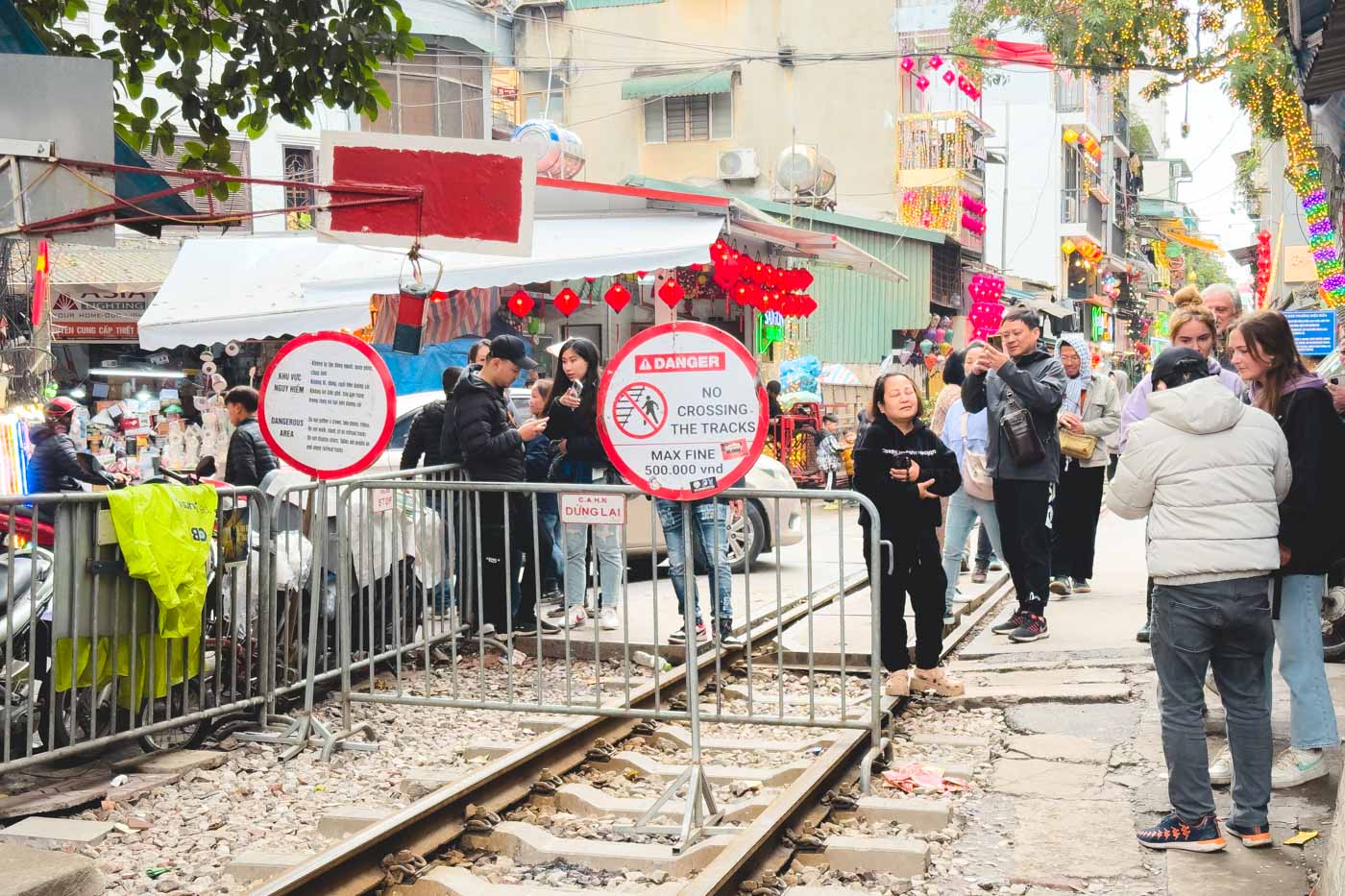 Tourists standing at the end of Hanoi Train Street beside a sign that warns people of a fine if they cross the tracks.