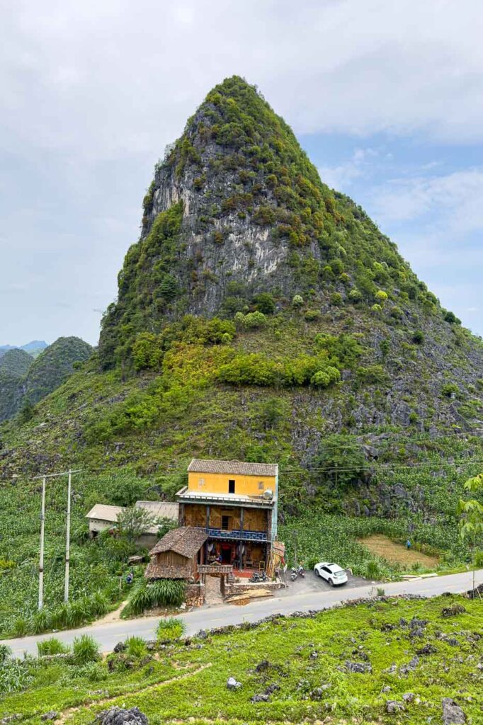 A little house along a road with a green mountain peak in the background.