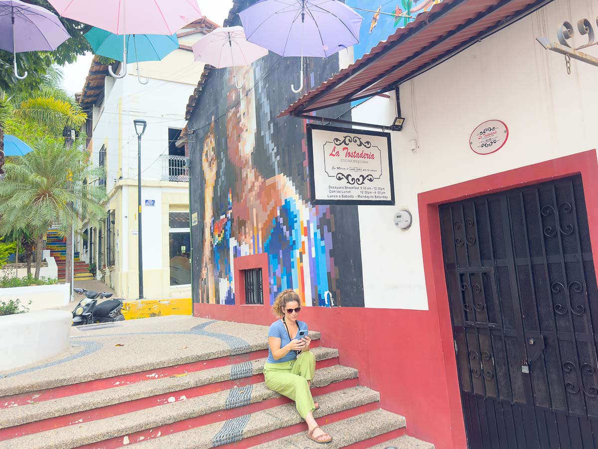 Nina on her phone sitting down on a colorful street.