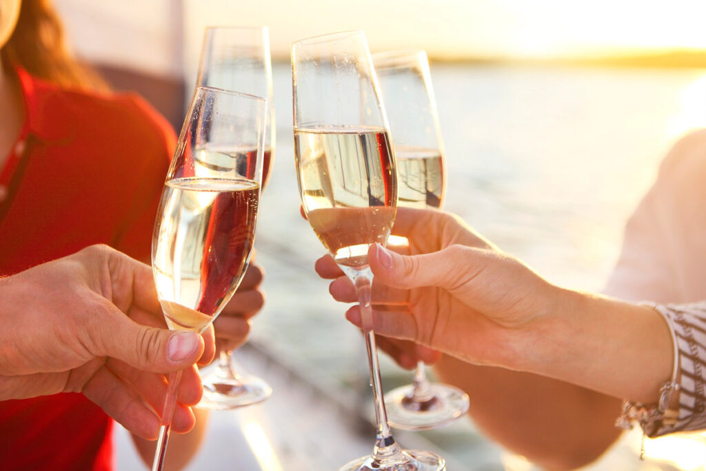 Happy friends with glasses of champagne on yacht. Vacation, travel, sea and friendship concept. Closeup.