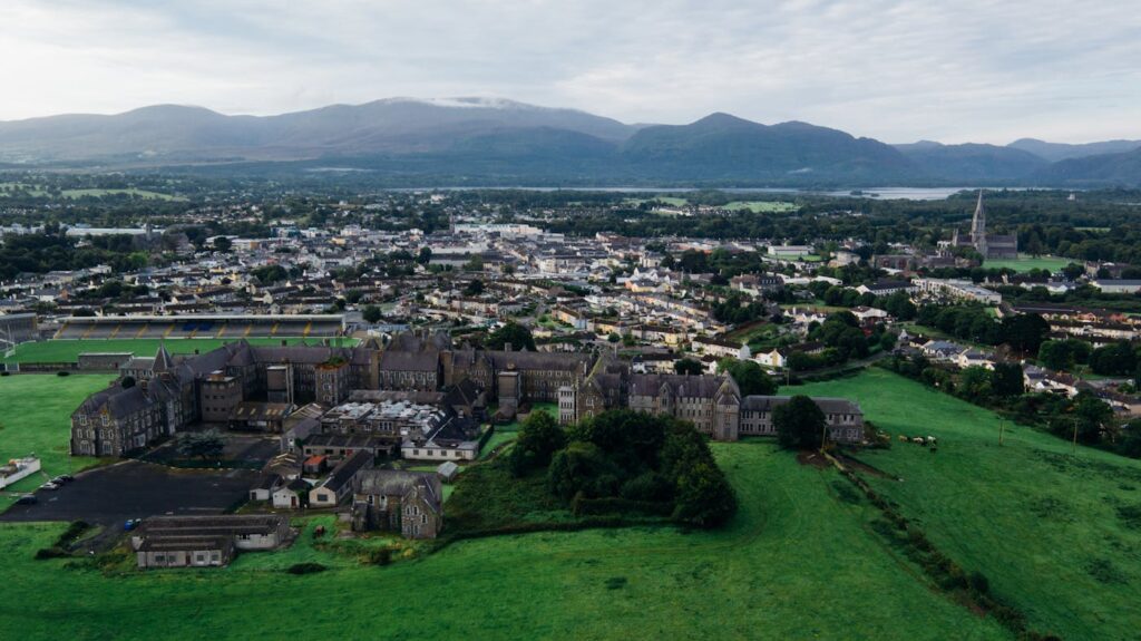 Scenic aerial view of a historic town surrounded by green fields and mountains in daylight.