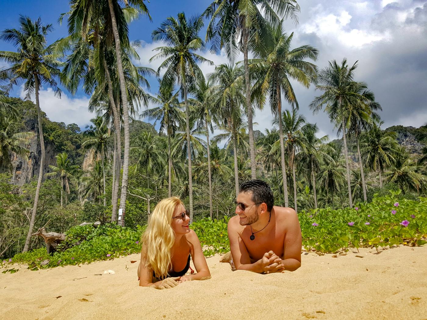 Couple enjoying a sunny day on a picturesque beach in Thailand surrounded by palm trees.