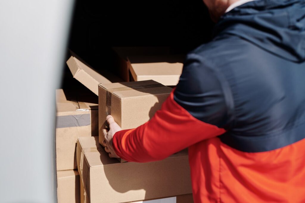 A delivery worker efficiently loads cardboard boxes into a vehicle for shipment.