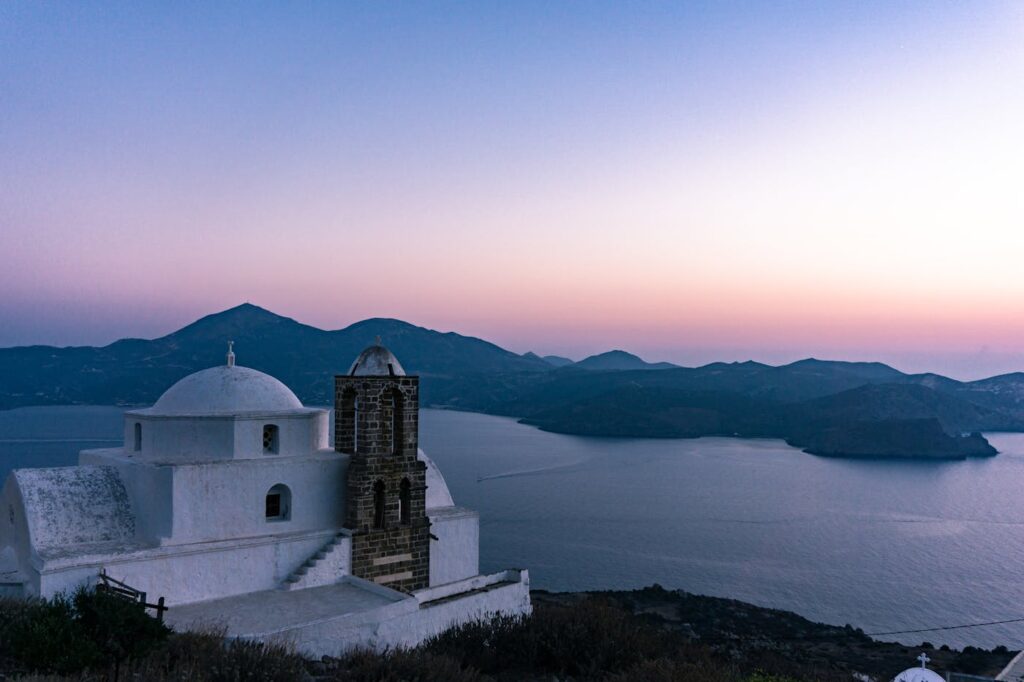 Captivating view of a white church in Milos, Greece, overlooking the serene ocean at sunset.
