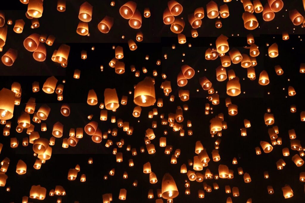 Hundreds of glowing sky lanterns float in the night sky, creating a magical and serene atmosphere.