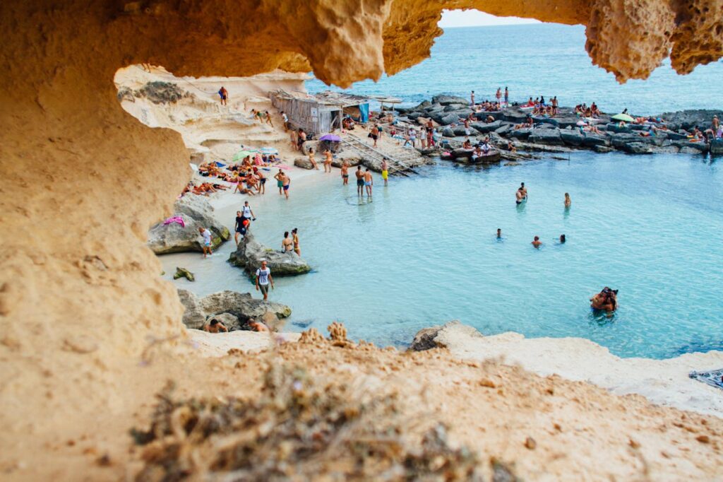 A picturesque beach scene in Spain with people enjoying swimming and sunbathing by rock formations.