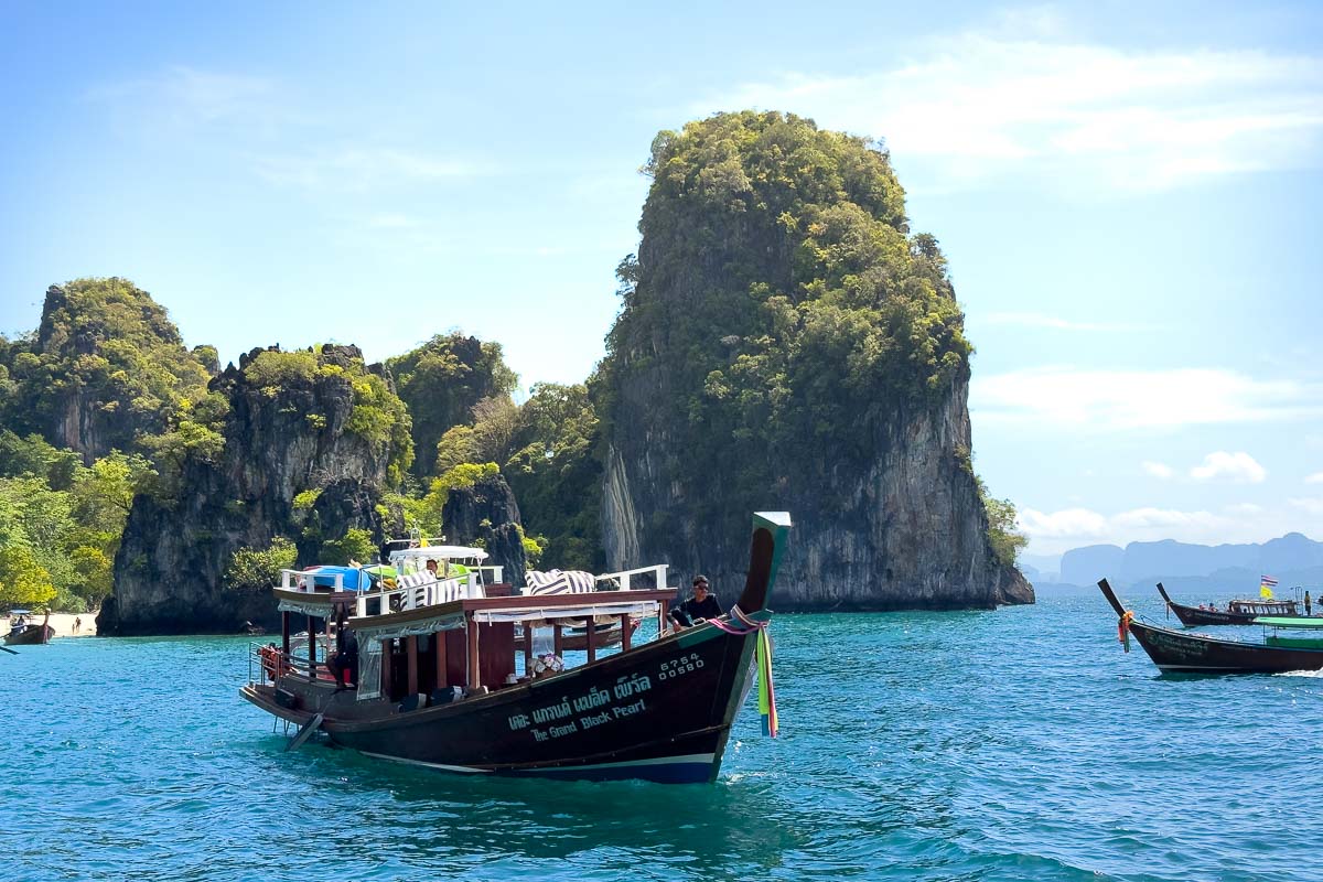 Big longtail boat with forested rocks behind it.
