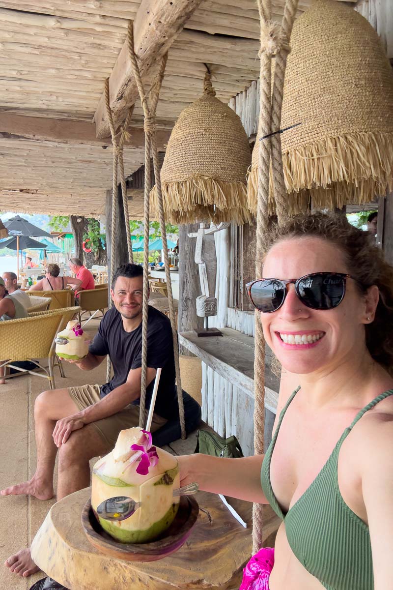 Nina and Garrett having coconuts at wooden bar on swing.