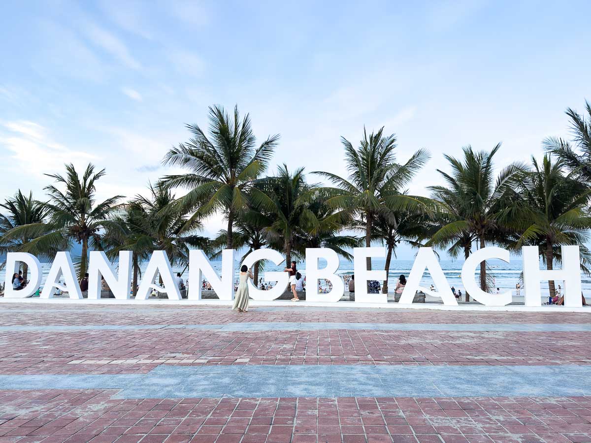 Many traditional Vietnamese fishing boats on the water besides rocks with a view of Da Nang in the distance. Da nang beach sign