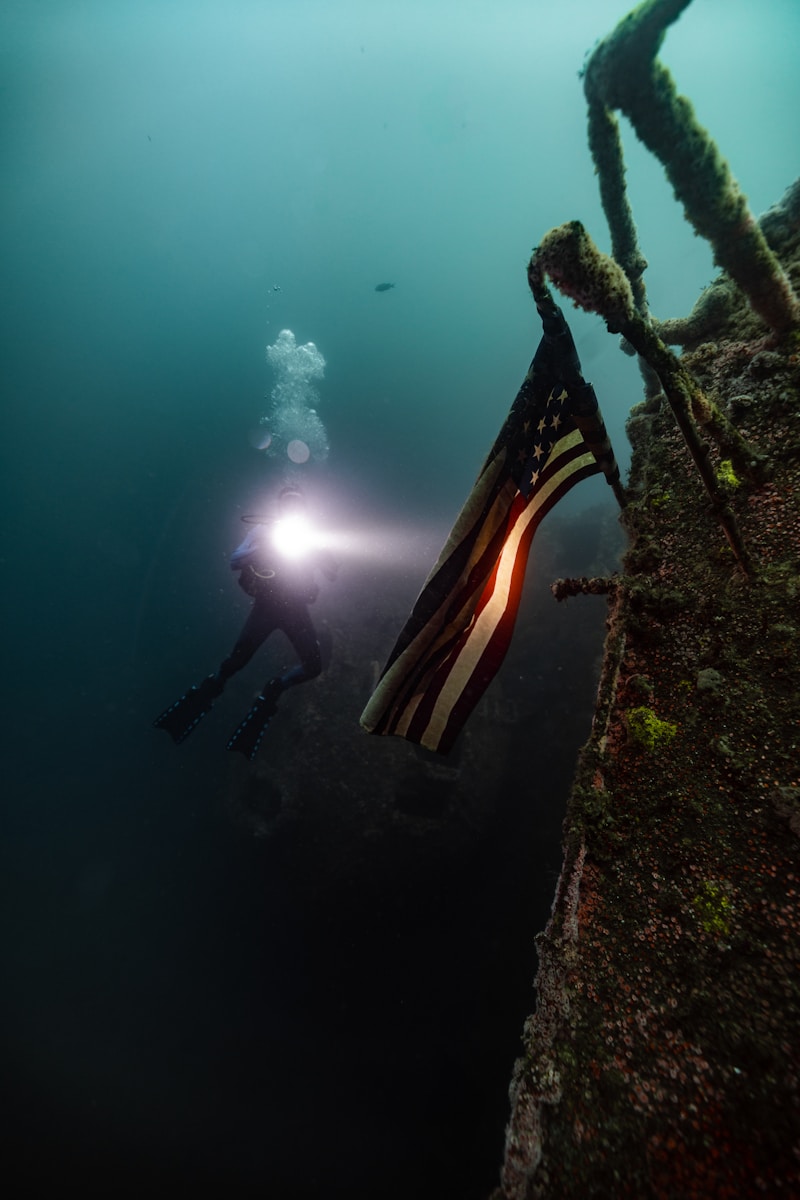 Scuba diver illuminating an american flag underwater.