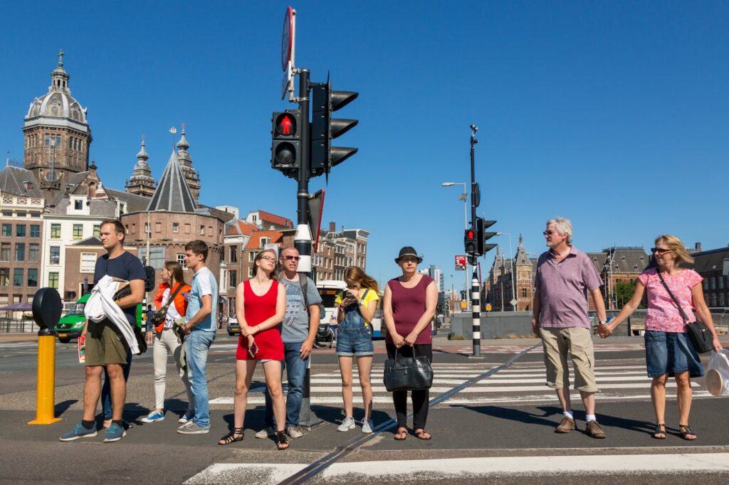 A group of people waiting at a crosswalk in front of historic buildings in Amsterdam, Netherlands.