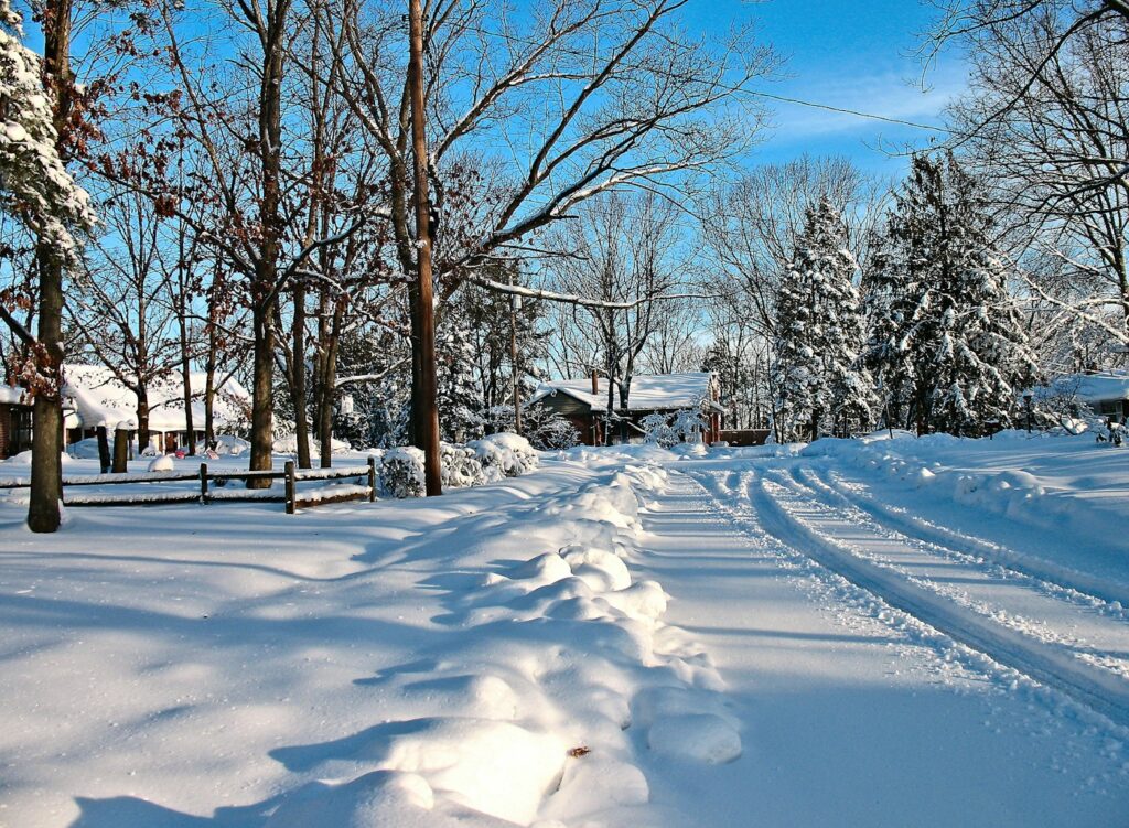 a snow covered road with trees and houses in the background