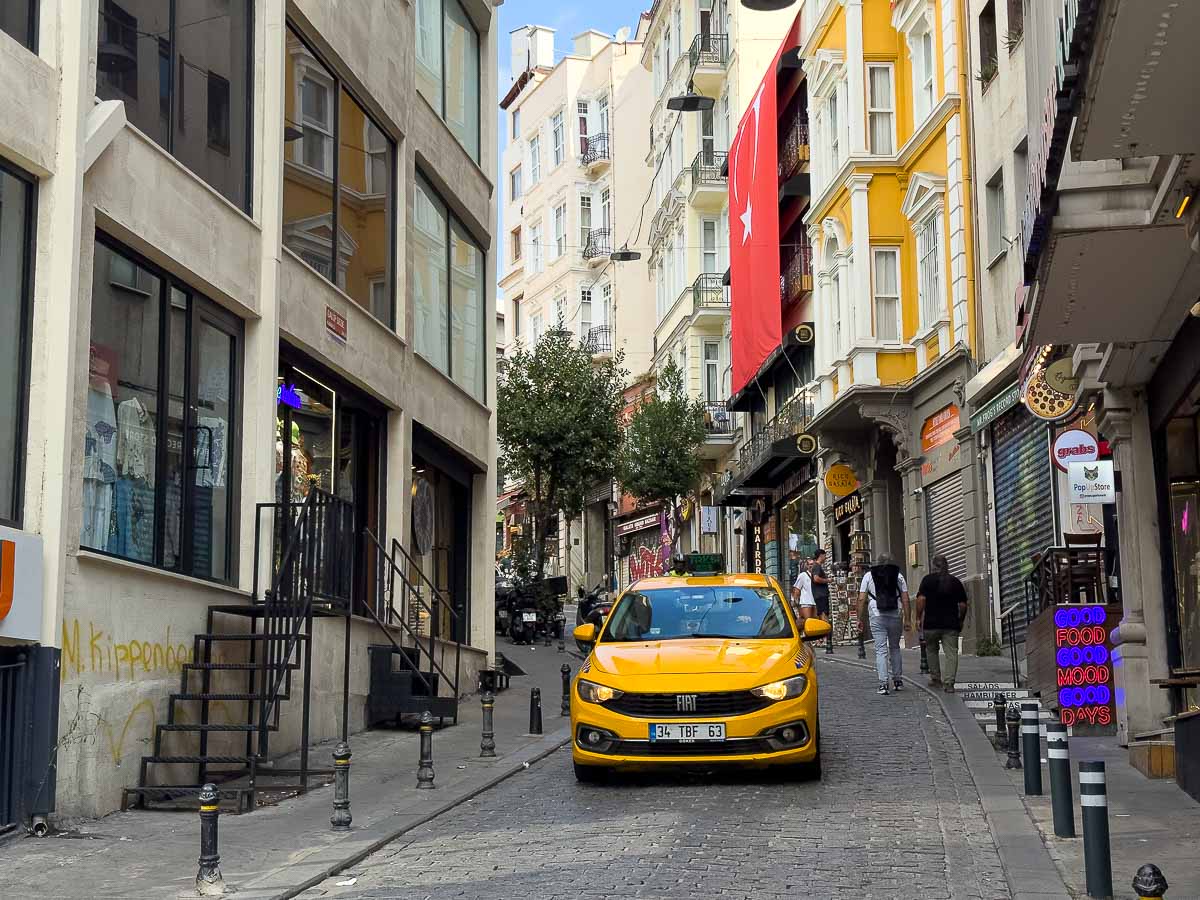 Yellow taxi with Turkey glad behind it driving down road.