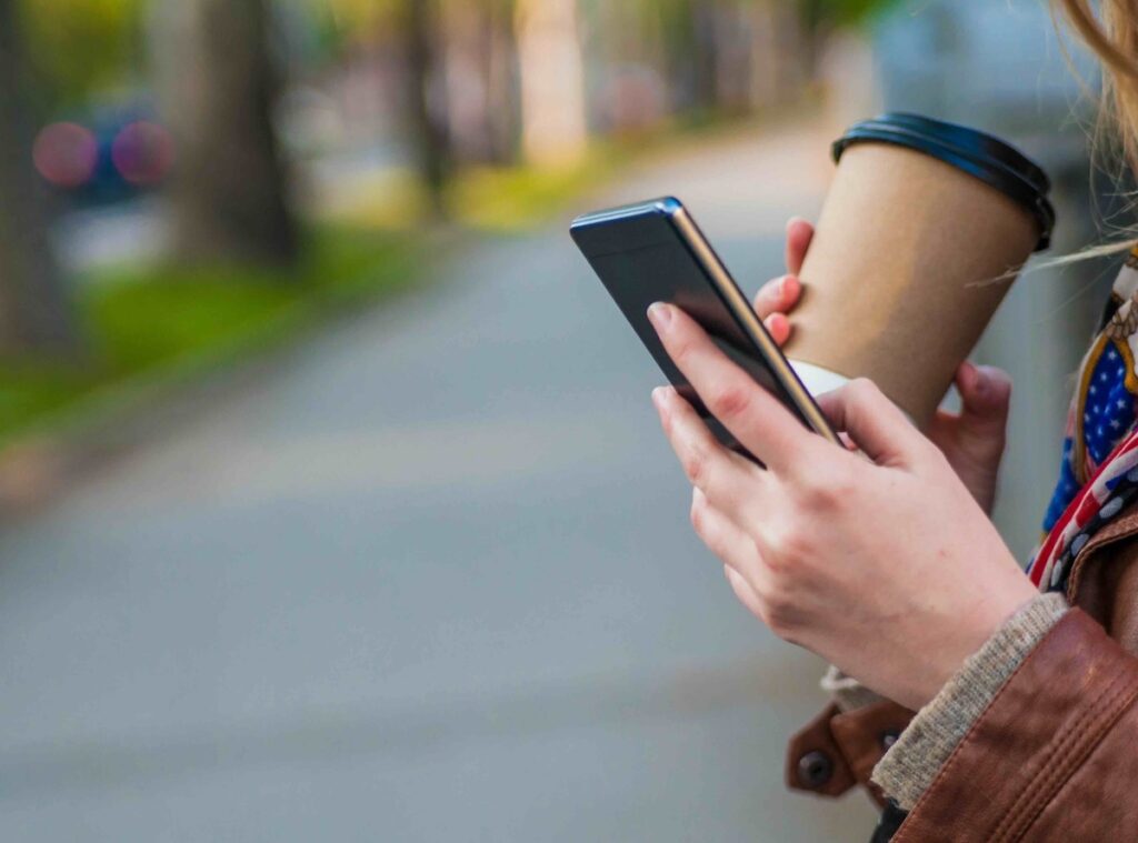 Close up of businesswoman checking email via mobile phone and holding a coffee cup. Hands with a coffee cup and mobile phone