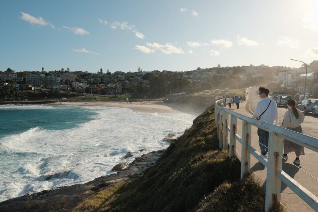 A couple of people walking down a road next to the ocean