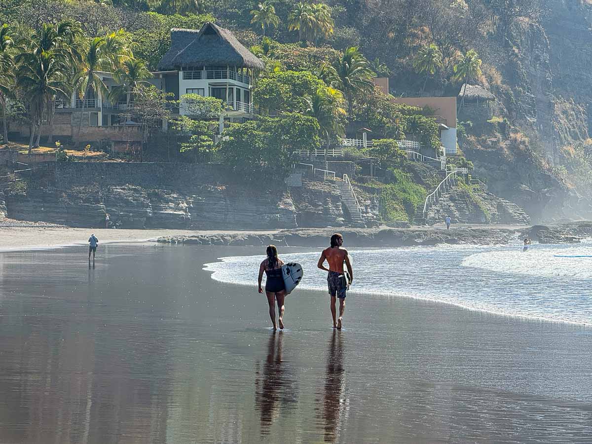 Two surfers walking along El Zonte beach.
