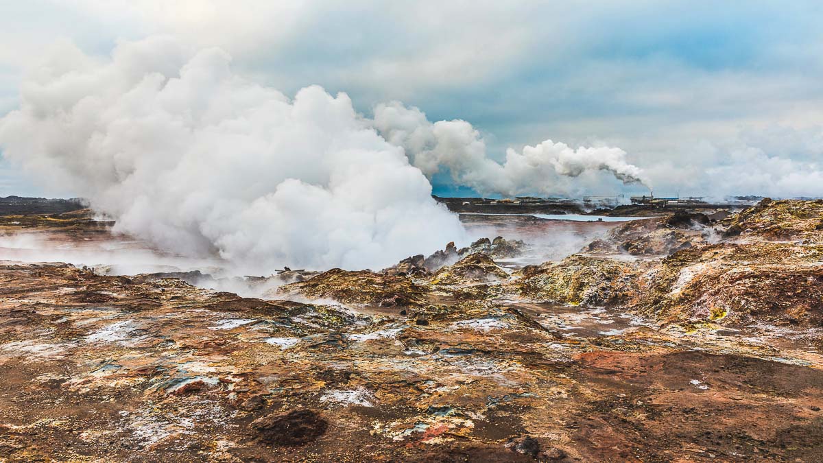 Gunnuhver hot springs in Iceland. Steam coming out from the earth and flowing over the ground. Geothermal power plants on background. Nature and industry concepts in Iceland