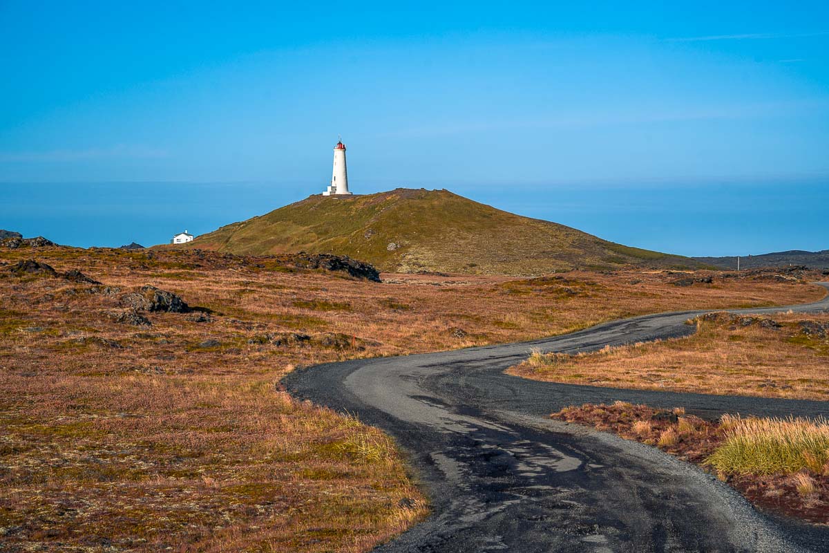 Reykjanes Lighthouse stands against a summer sky, surrounded by steaming Gunnuhver hot springs on Iceland’s rugged coastline