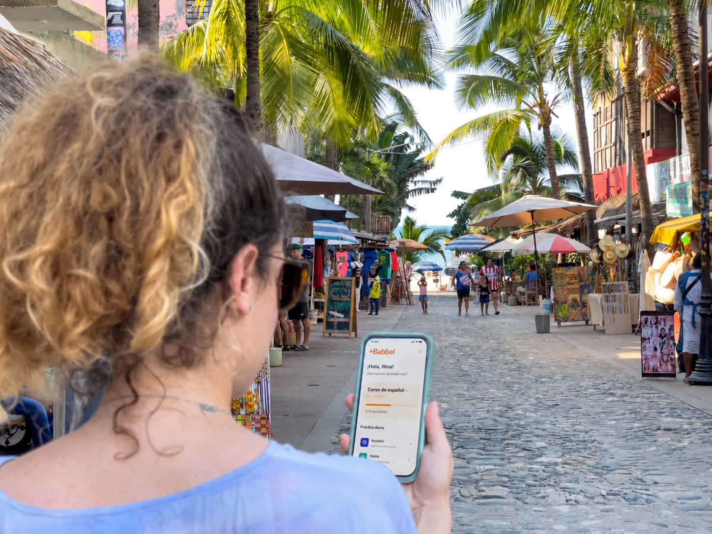 Nina using Babbel app in Mexico street with palms.