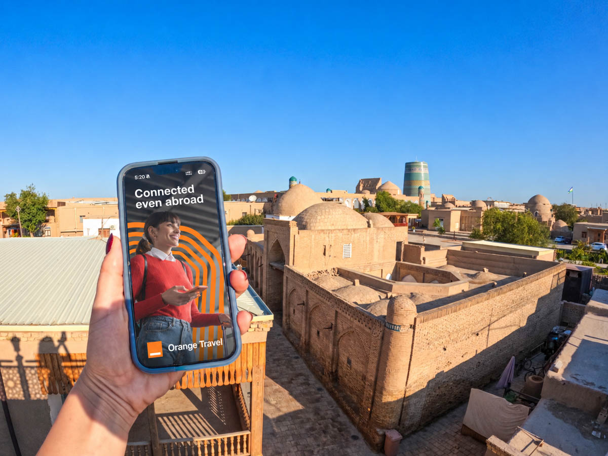 orange travel esim app open on phone with Khiva, Uzbekistan buildings behind it.