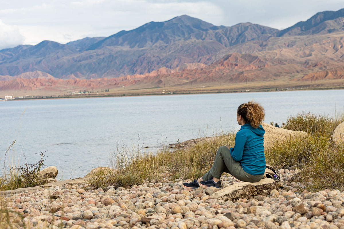 Nina sitting at the edge of Issyk-Kul Lake with mountains behind, Kyrgyzstan
