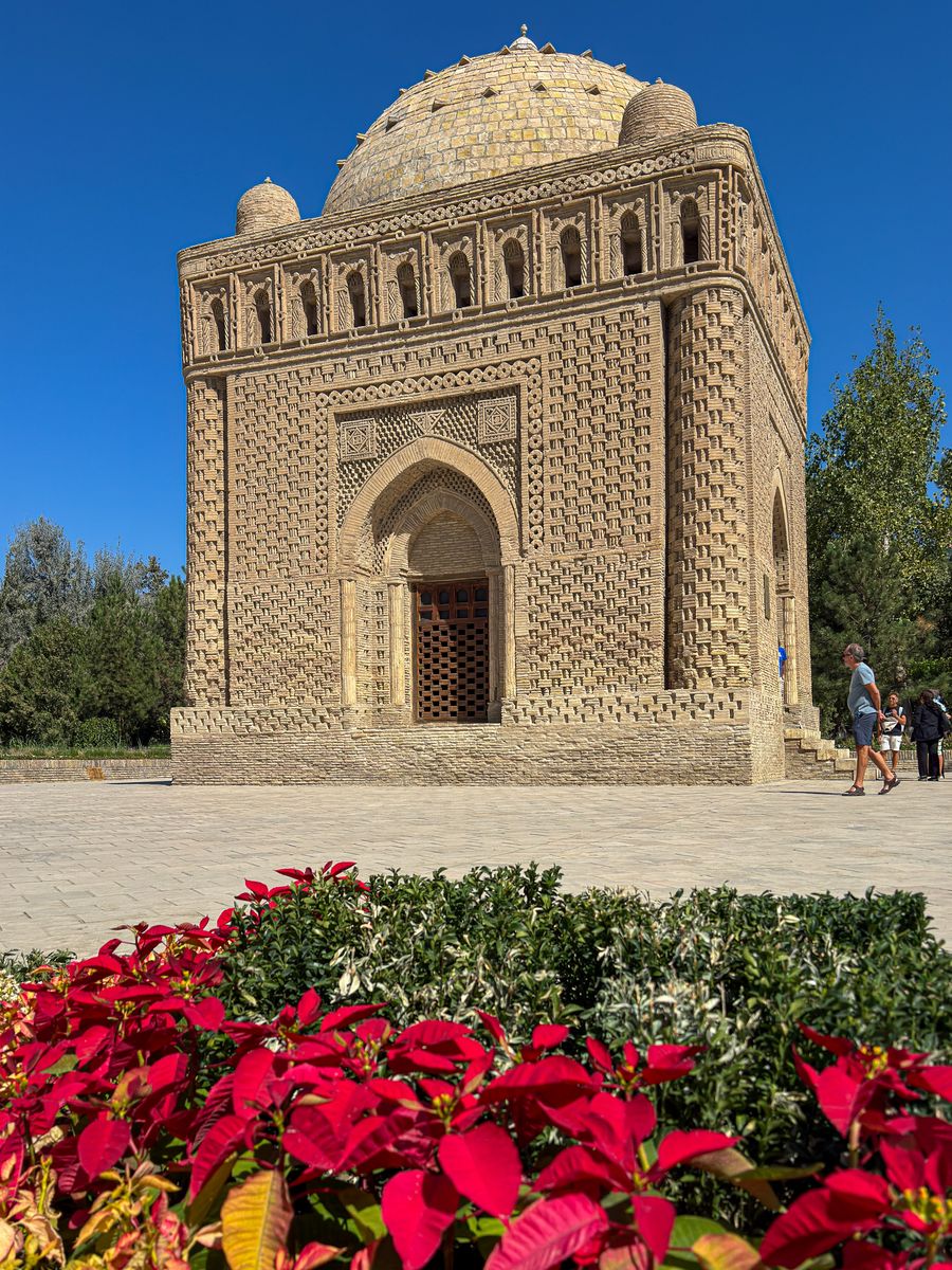 The brick Samanid Mausoleum with red flowers in front, Bukhara, Uzbekistan